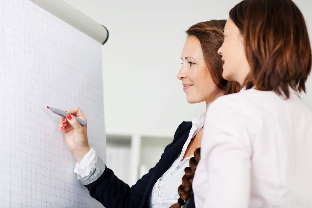 Two ladies talk business while working with the white board