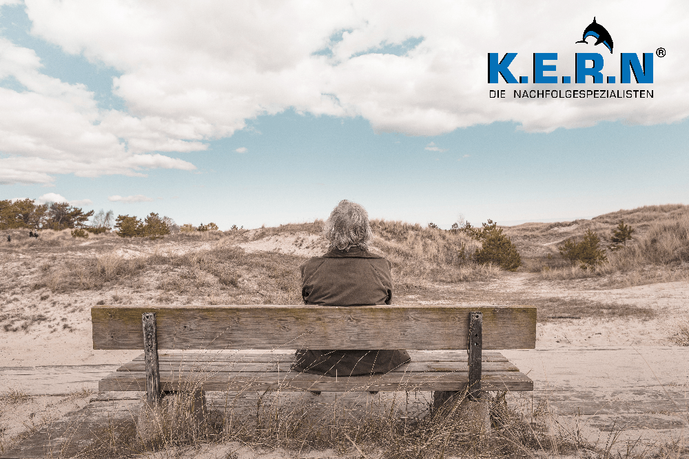 Senior sitting on a bench in the dunes of the Baltic Sea, the KERN logo in the top right-hand corner.