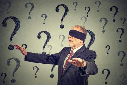 Ein Mann mit Augenbinde irrt durch einen Raum voller Fragezeichen
