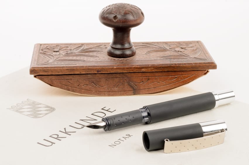 Akt notarialny na biało-żółtym papierze z leżącą na nim pieczęcią i wiecznym piórem