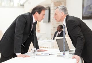 Two businessmen face each other with a competitive look at the table